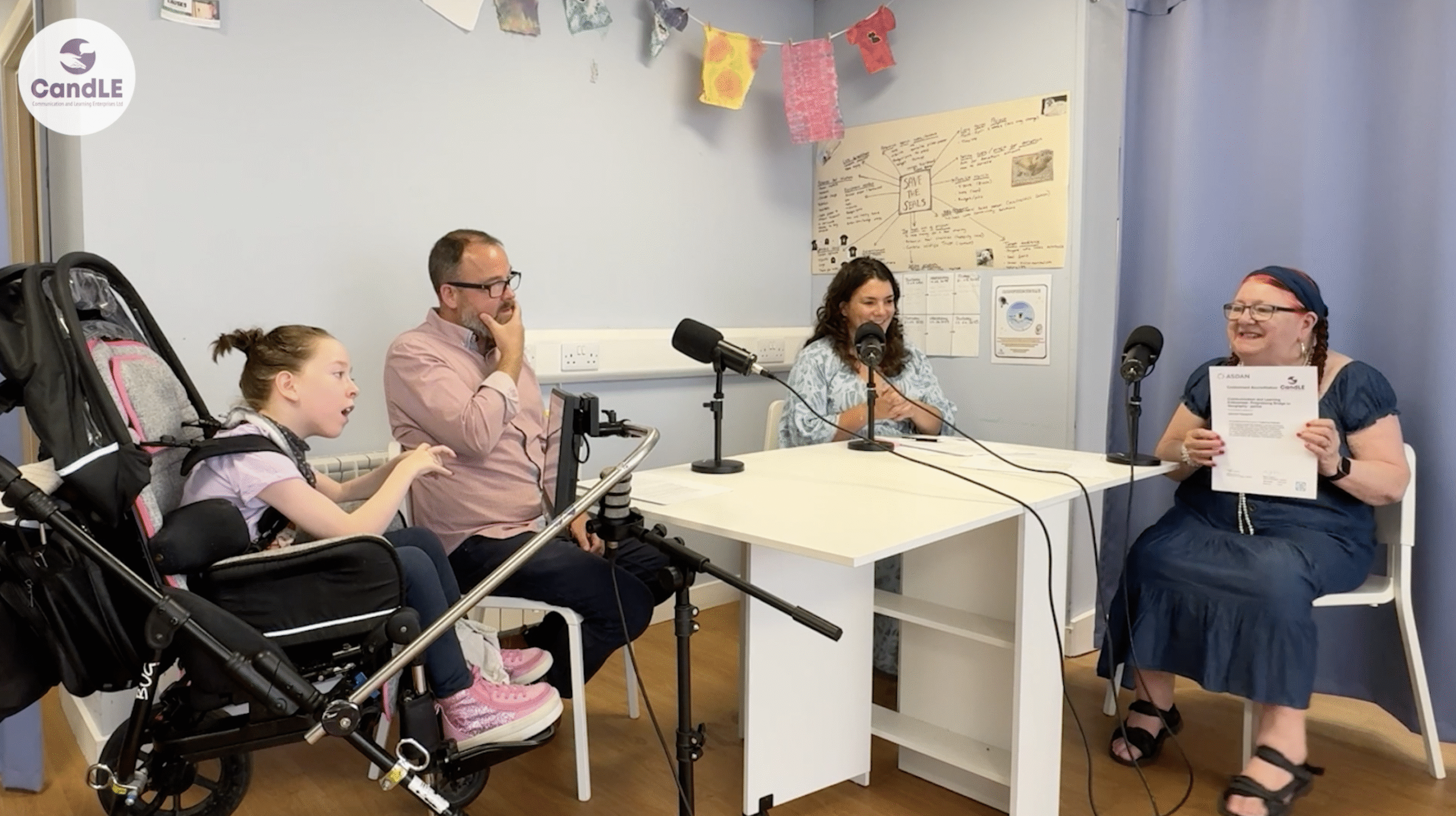 CandLE Podcast episode 2 image Image of podcast episode. Features disabled student being given a certificate by a teacher. She is sitting with her dad and two specialist teachers around a table with microphones.